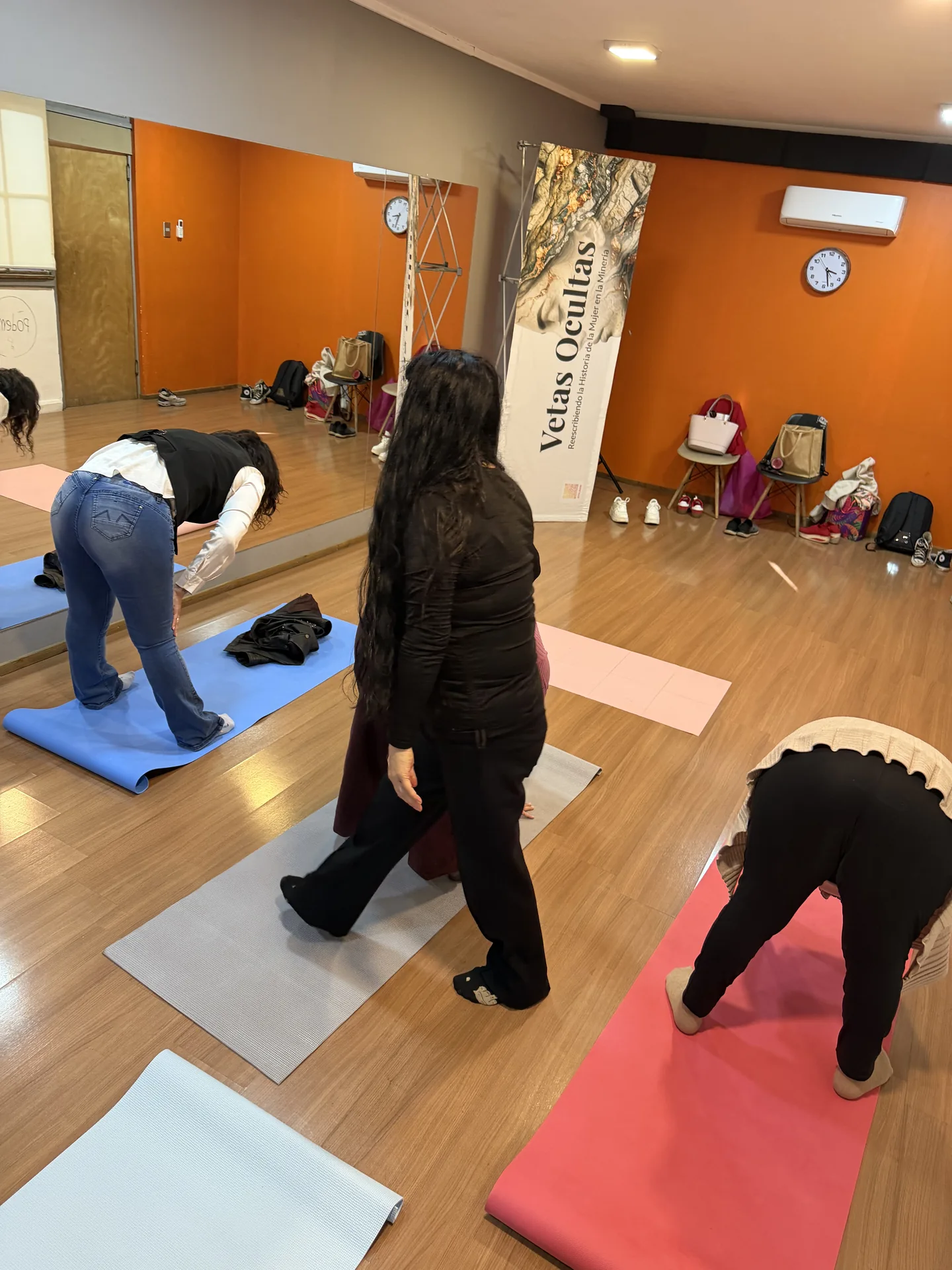 Participantes del taller en sala con colchonetas, realizando ejercicios de comunicación corporal bajo la guía de la relatora, con el banner de Vetas Ocultas al fondo